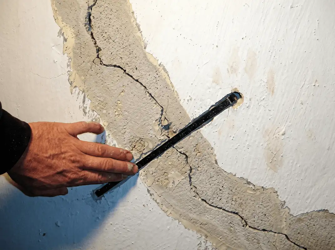 A wall with a large crack is being inspected by a professional in Tampa, FL