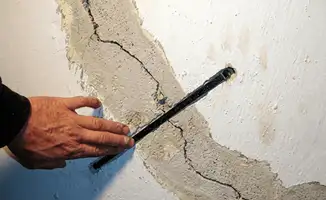 A wall with a large crack is being inspected by a professional in Tampa, FL